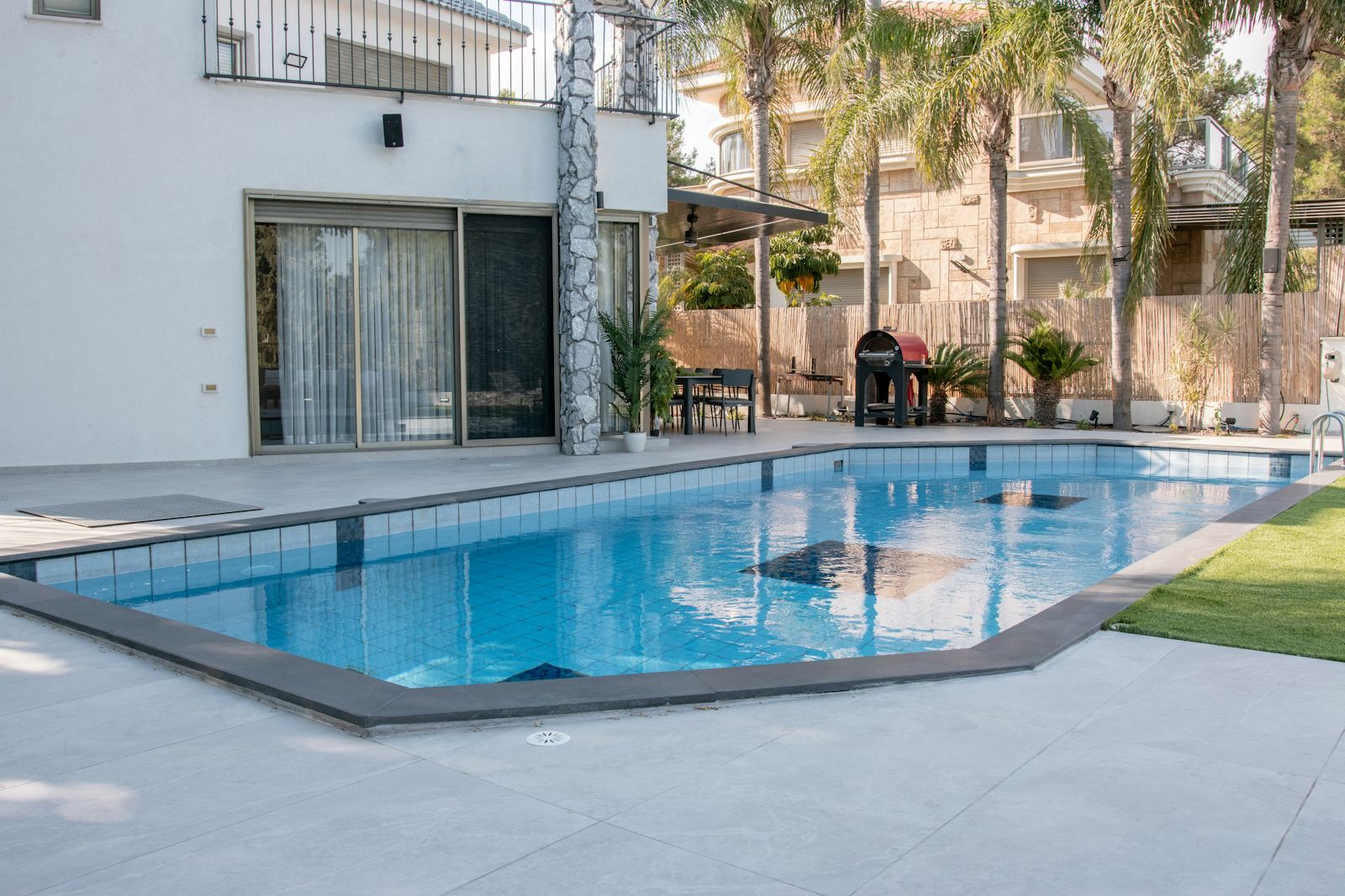 Backyard swimming pool with a stone deck and palm trees